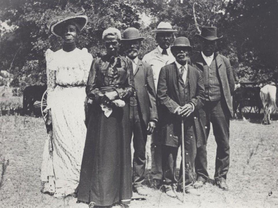 a black and white image of a group of well-dressed Black men and women posing outside at an Emancipation Day Celebration, 1900, Austin History Center.