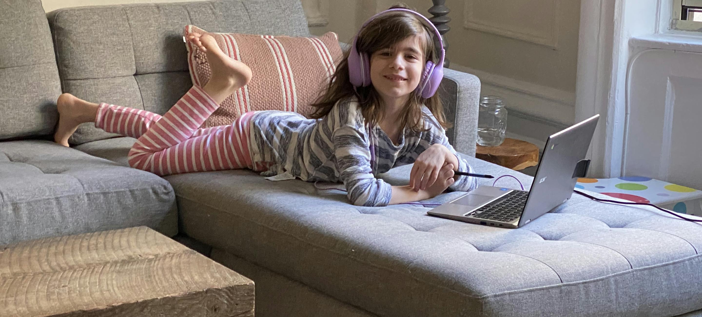 young white girl wearing headphones, laying on a couch and interacting with a computer