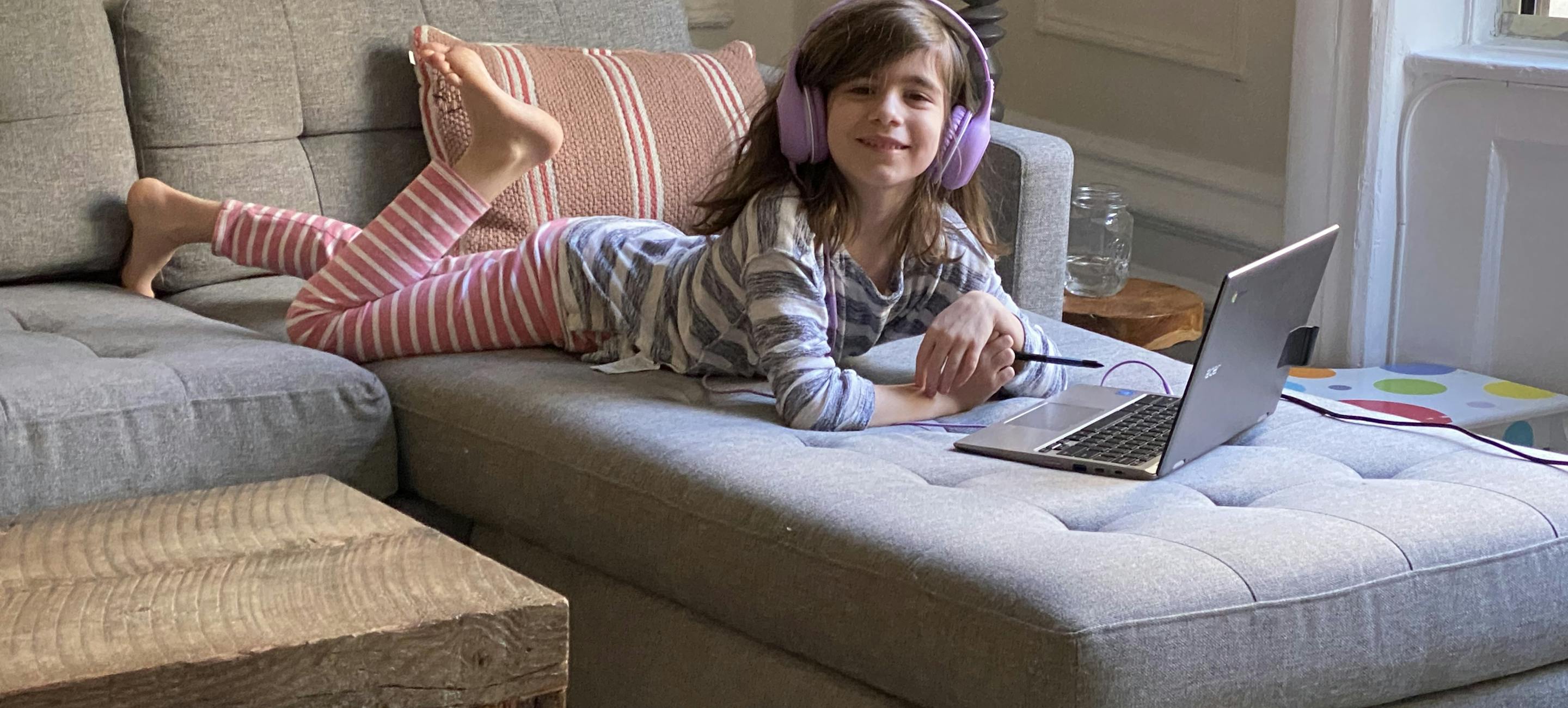 young white girl wearing headphones, laying on a couch and interacting with a computer