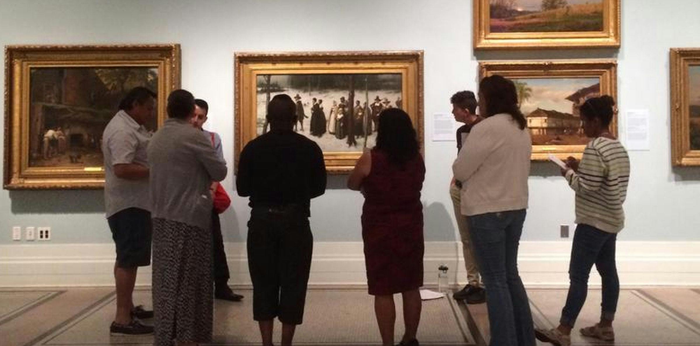 group of museum-goers circled around a painting in a gallery room