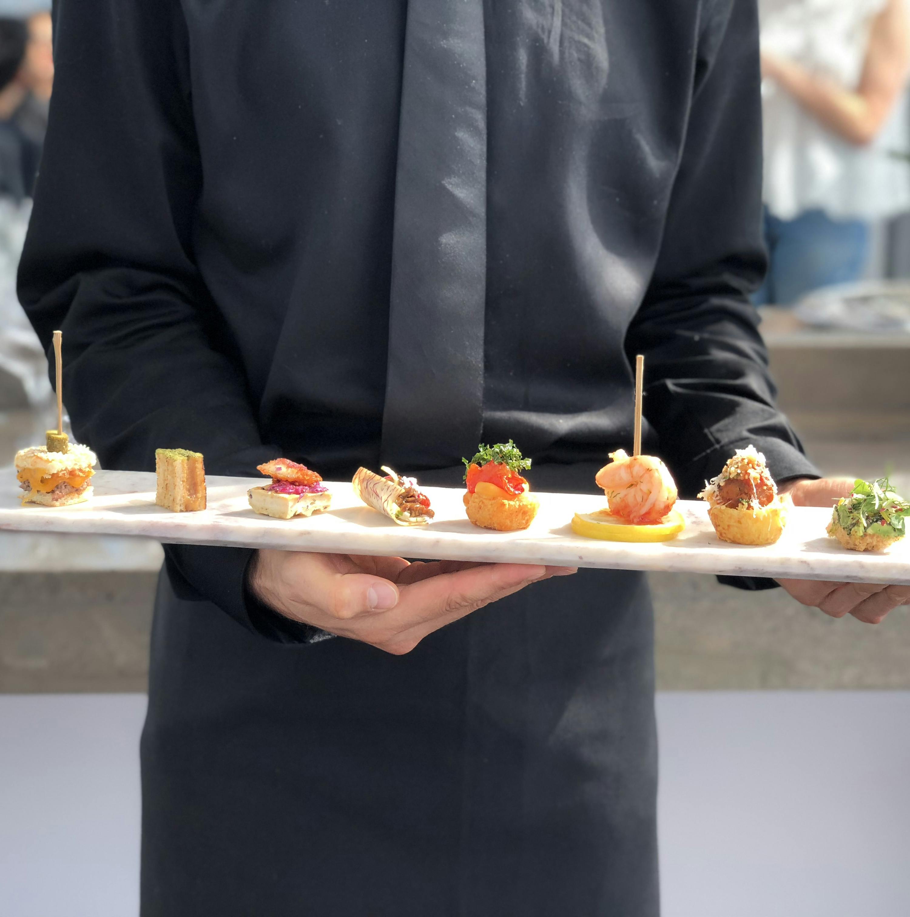 a black-clad server holding a tray of passed appetizers