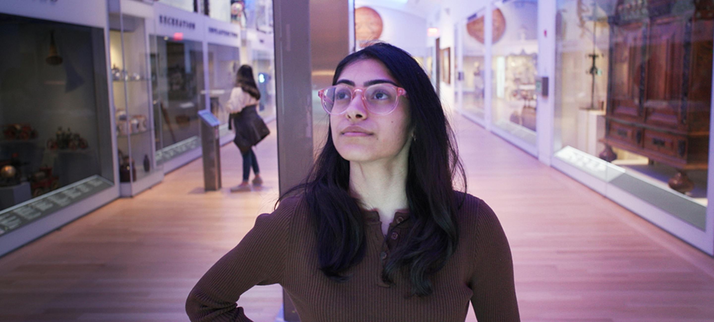 a woman with long dark hair wearing glasses looks at a niche in objects tell stories