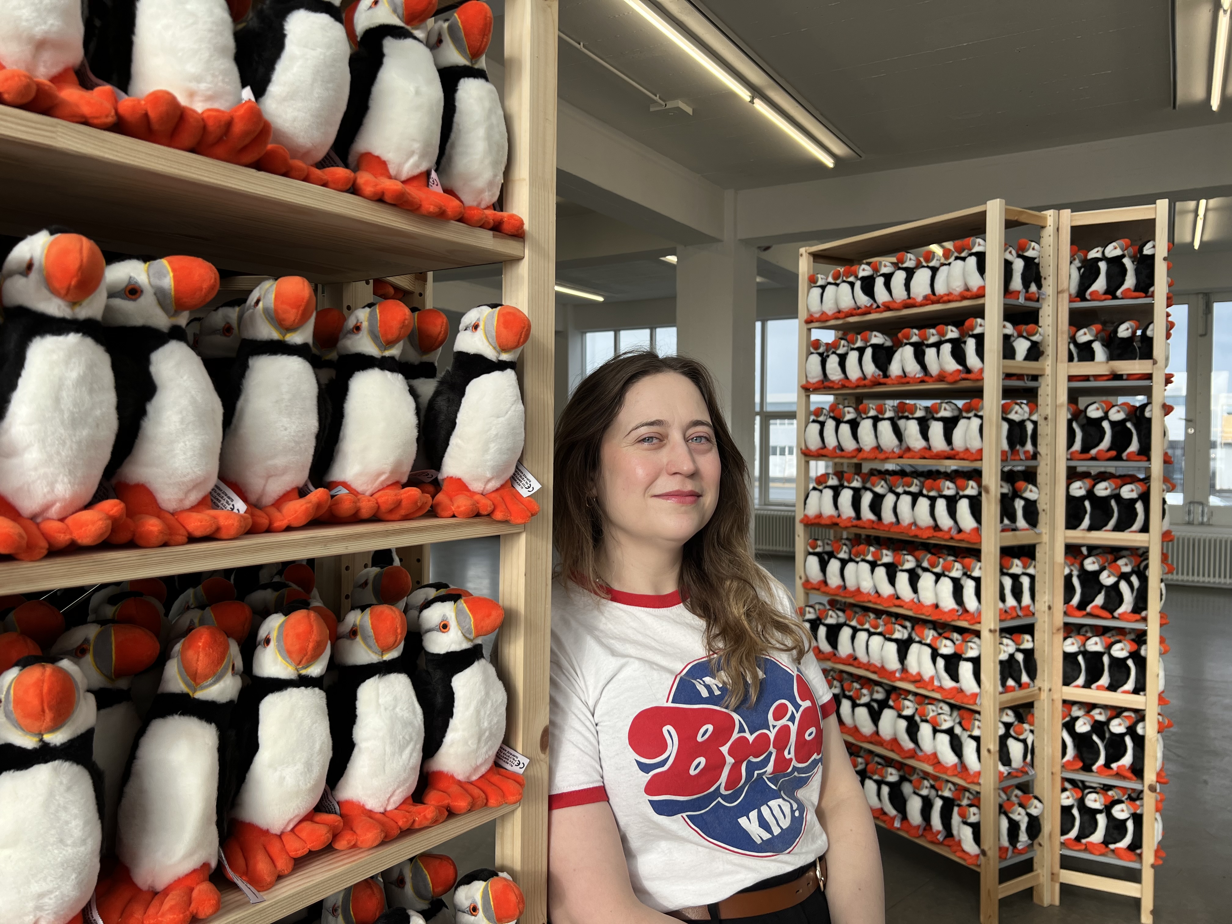 A woman standing next to shelves full of stuffed puffins.