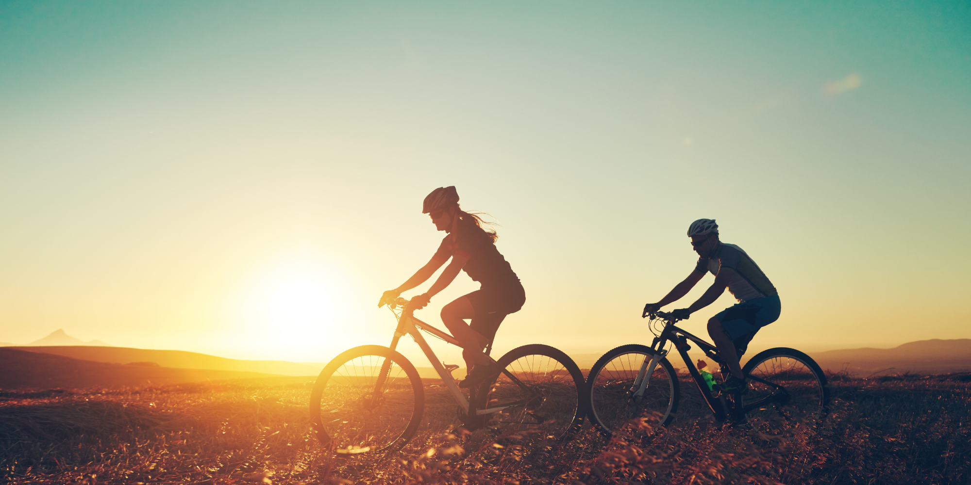 the sillhoette of 2 people cycling infront of a sunset