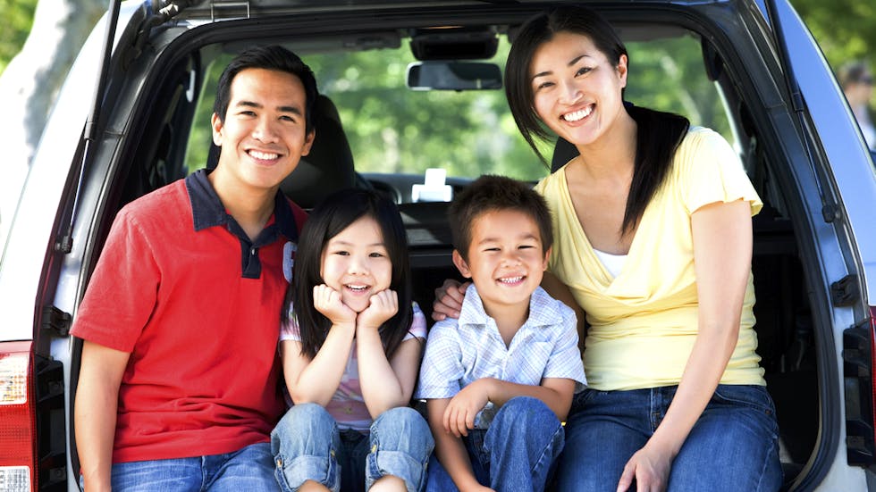 Familia asiática sentados en el maletero de un monovolumen