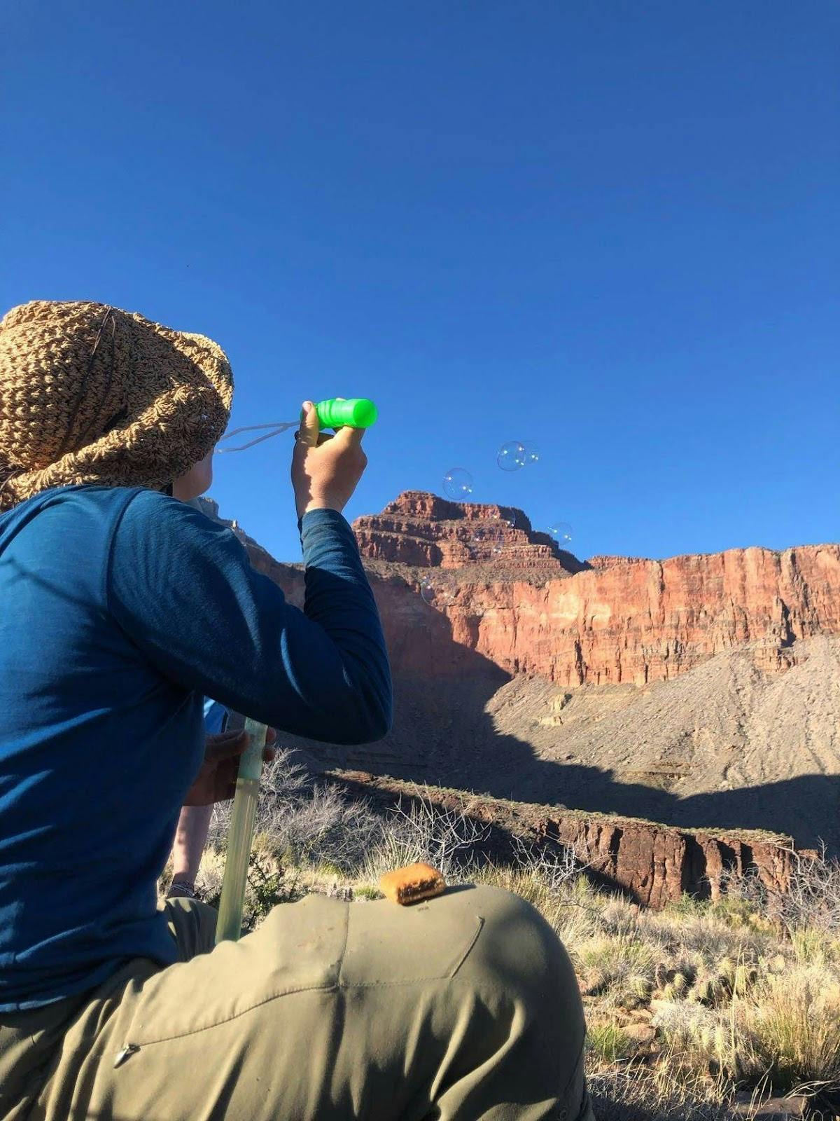 Hiker blowing bubbles with butte in the background on a sunny mountain day.