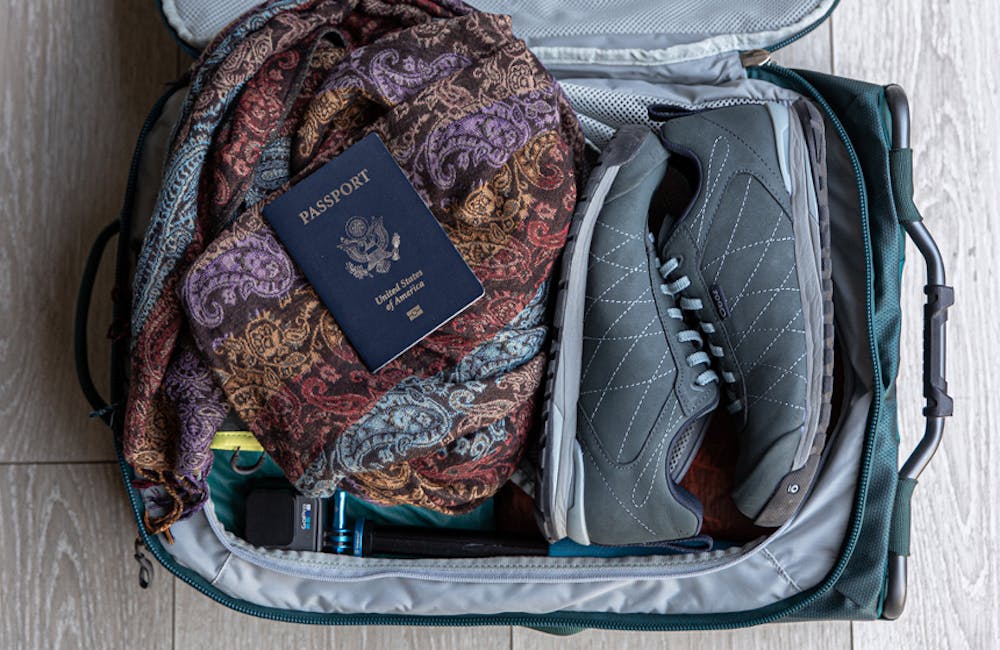 Suitcase zipped open with the Women's Bozeman Low shoes, a scarf and a passport