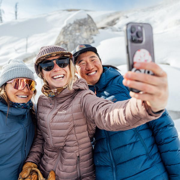 Three friends taking a selfie together at Yellowstone National Park in front snowy backdrop.