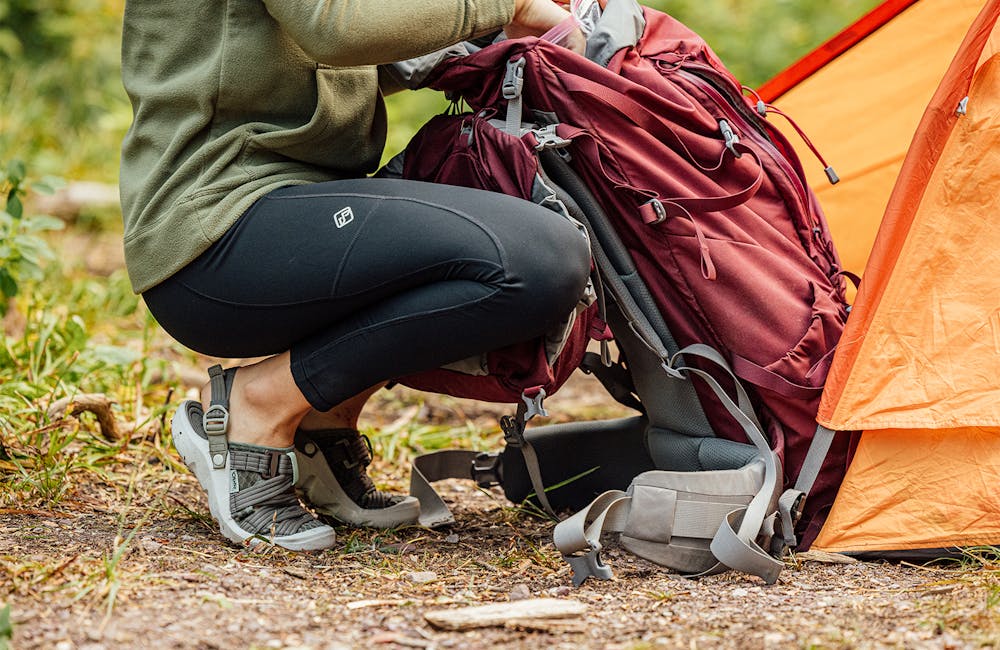 A woman unpacks a backpack in camp wearing Oboz footwear