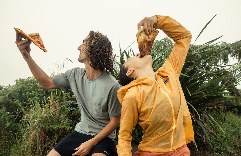 Two people enjoying pizza on a hike during a rain storm.