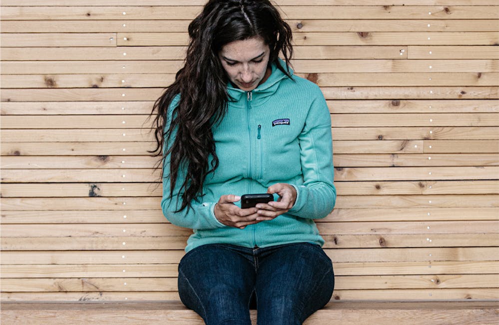 Jackie Nourse sitting on a bench on her phone wearing her Oboz shoes