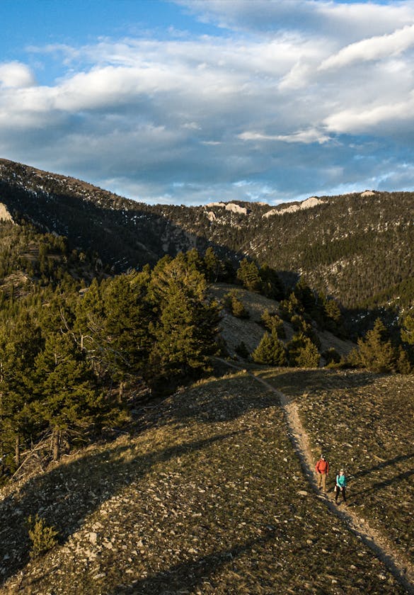 Two hikers in Montana mountains walking up a dirt trail in Oboz hiking boots..
