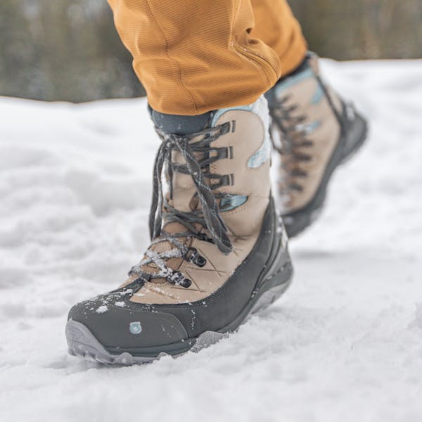 Oboz Ousel insulated winter boots walking over a hard packed snowy trail.