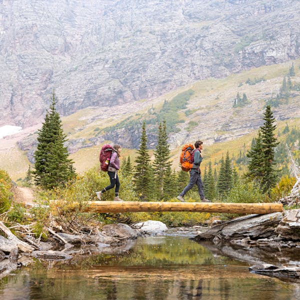 Two backpackers hiking across a bridge through Montana wilderness.