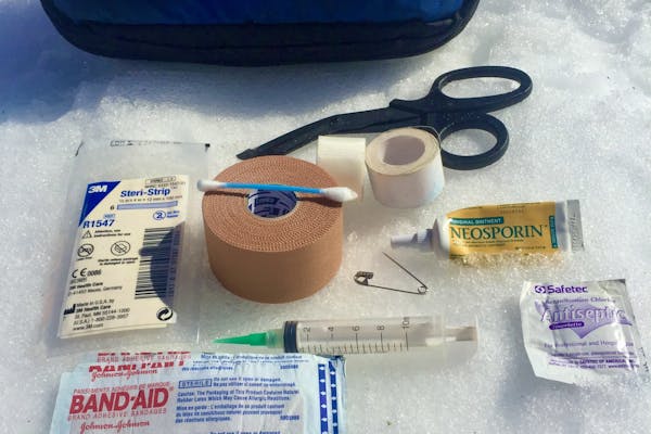 First Aid kit placed on snow to show the recommend essentials one should carry