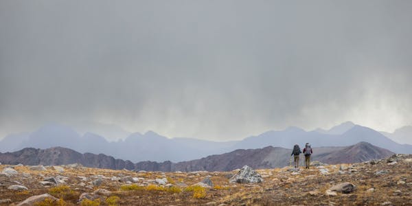 Two hikers wearing Oboz Bridger Mid hiking boots heading into a storm in the high Colorado alpine.