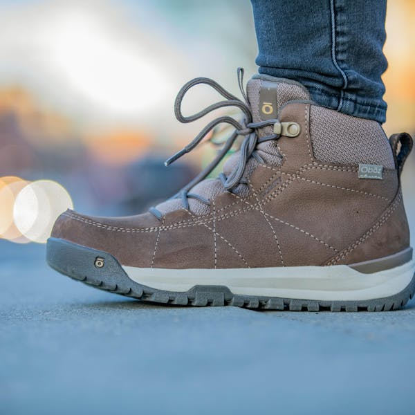 A woman wears a pair of Oboz Cedar winter boots on a paved sidewalk.