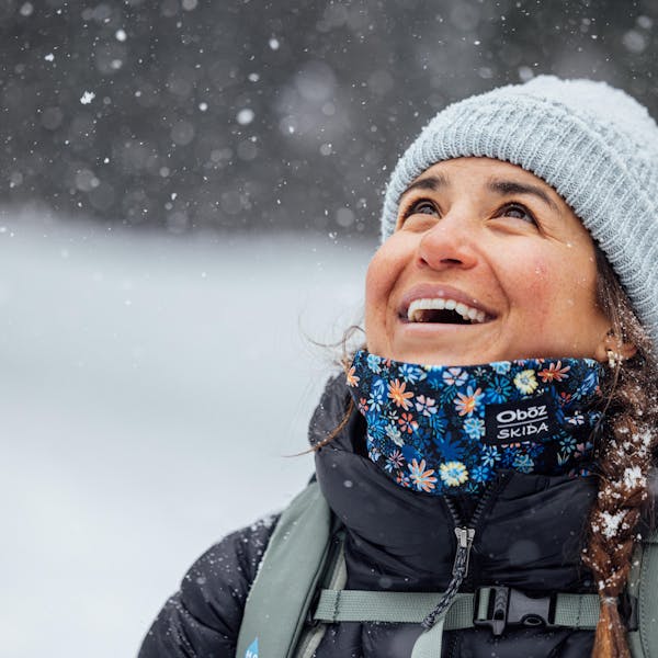 Woman laughs in the snowy winter weather while hiking in an Oboz X Skida neck warmer.