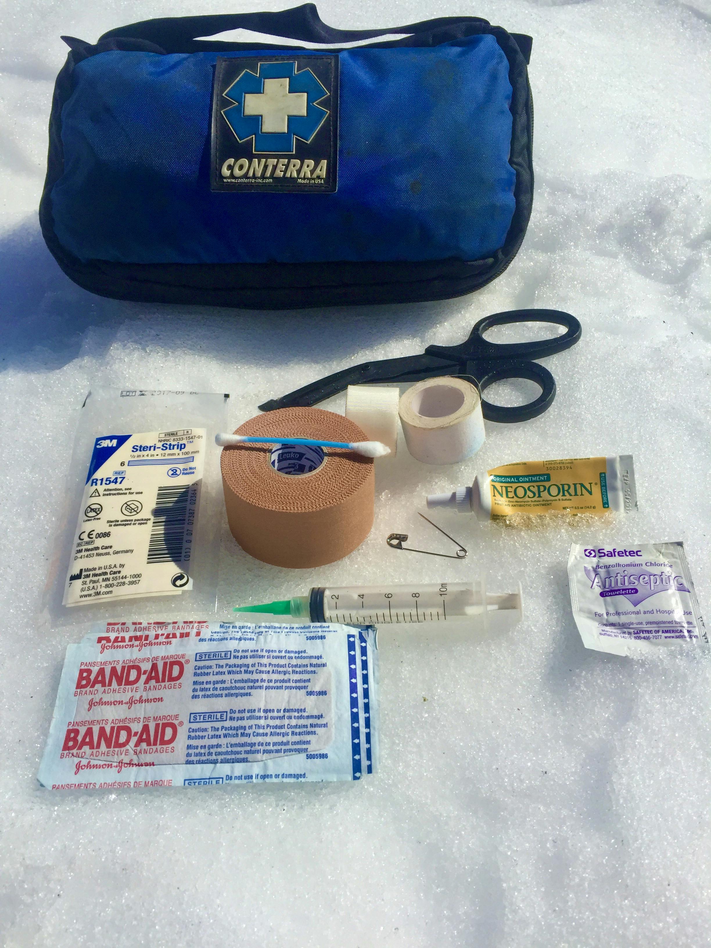First Aid kit placed on snow to show the recommend essentials one should carry