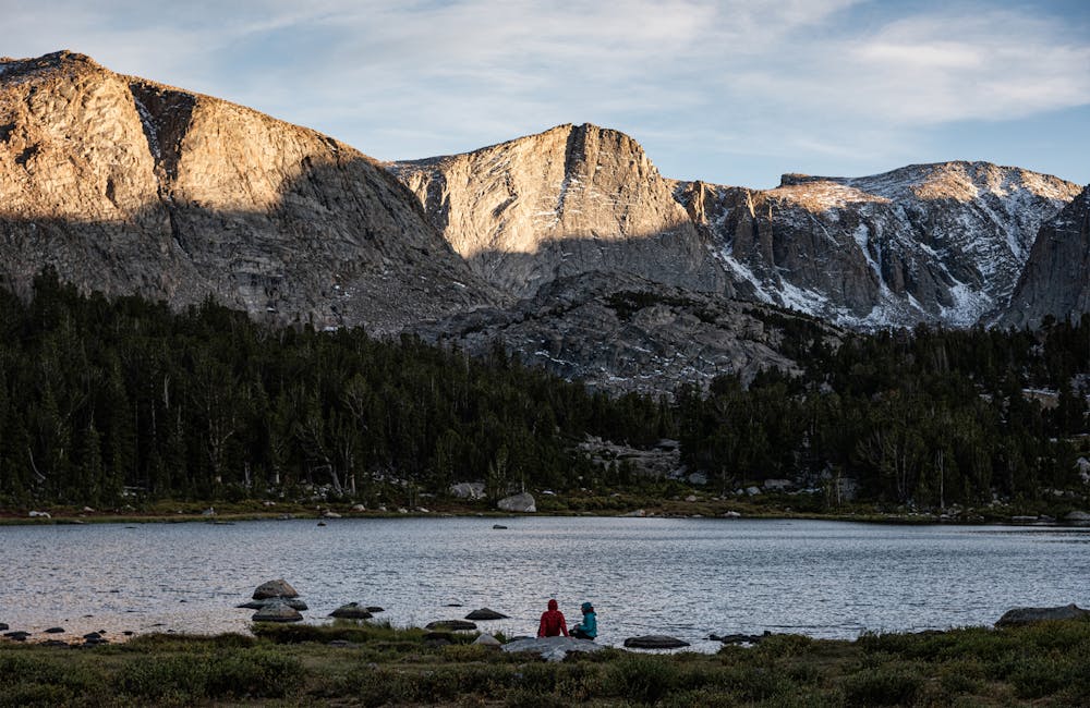 Two backpackers relaxing in front of a mountain lake.