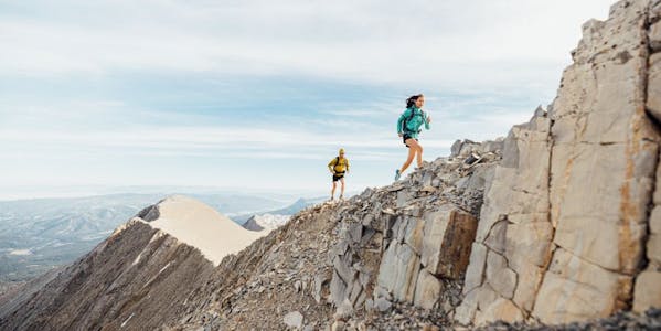 Two people run up a rocky ridge in a blue and yellow jacket wearing Oboz Katabatic trail shoes. 