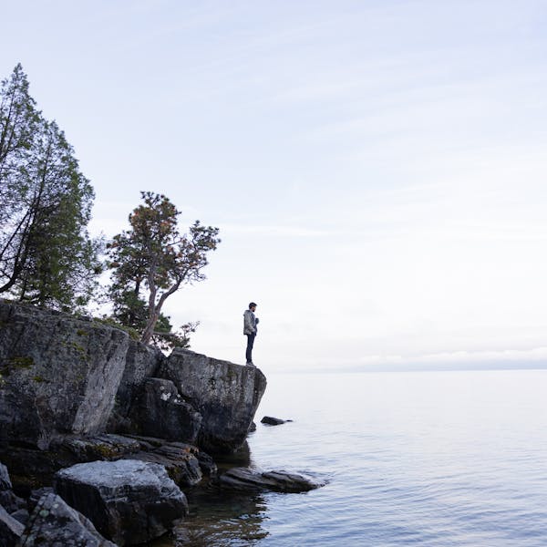 A person standing on a rocks edge looking out into the water.