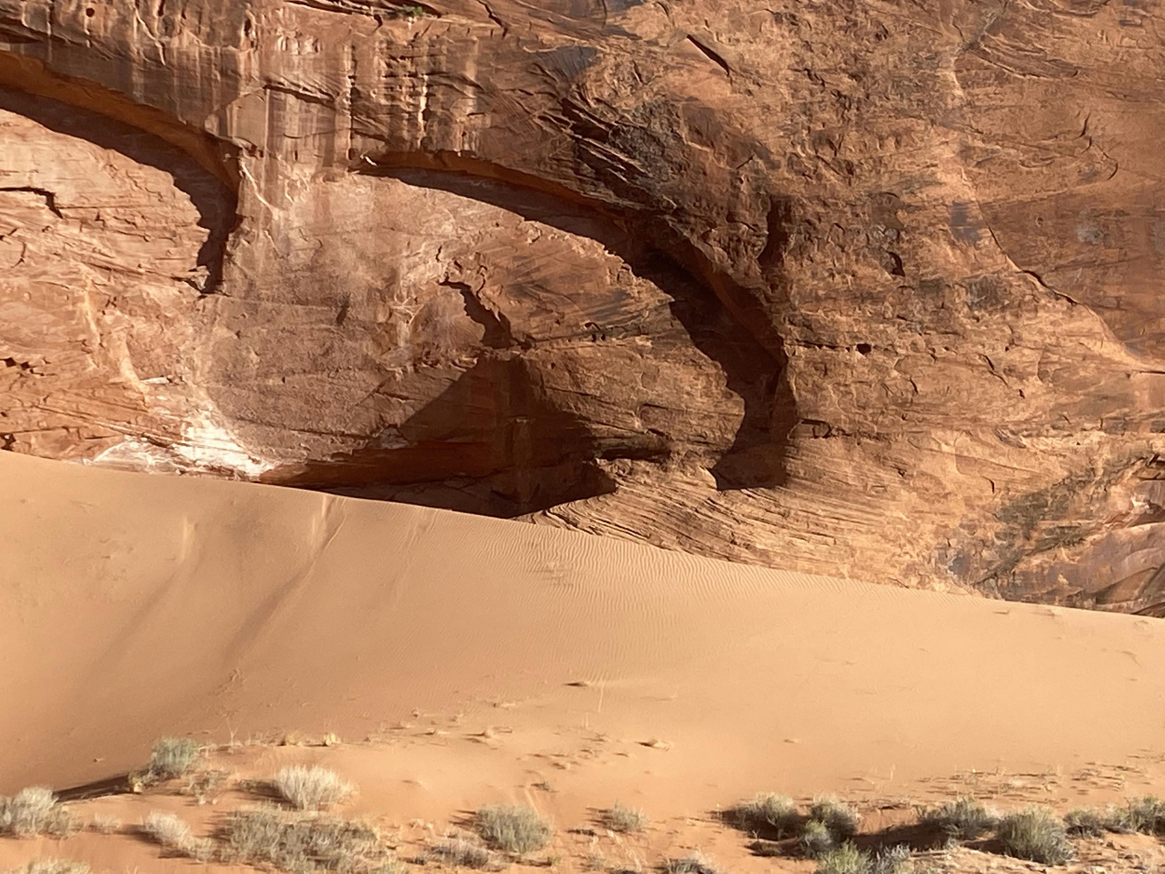 A desert sand dune under a massive red rock.