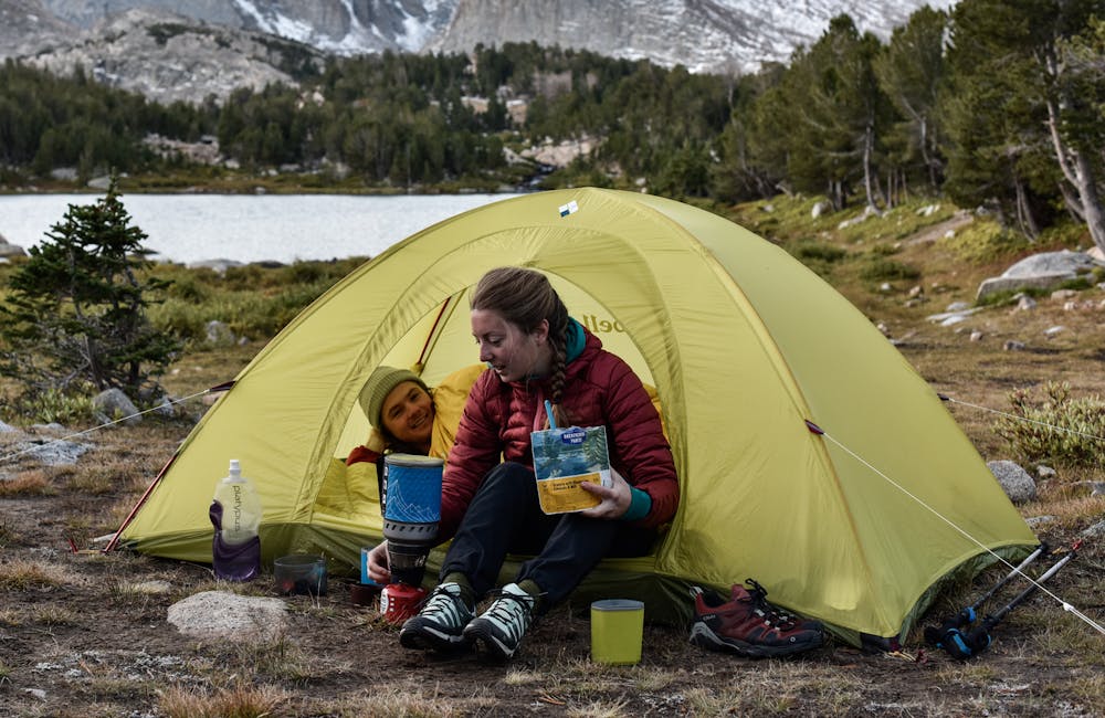 Two backpackers in a tent preparing a jetboil meal while wearing the Oboz Arete hiking shoes.