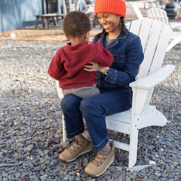 Woman sits in chair outside, smiling with a child in her lap wearing Oboz Hazel shoes