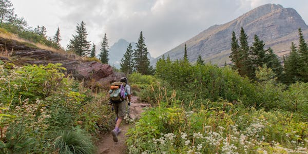 Hiker walking through lush mountain meadow surrounded by mountain peaks.