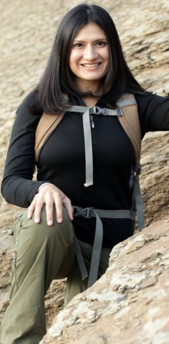 Karla Amador standing along a rock wall wearing Oboz hiking shoes
