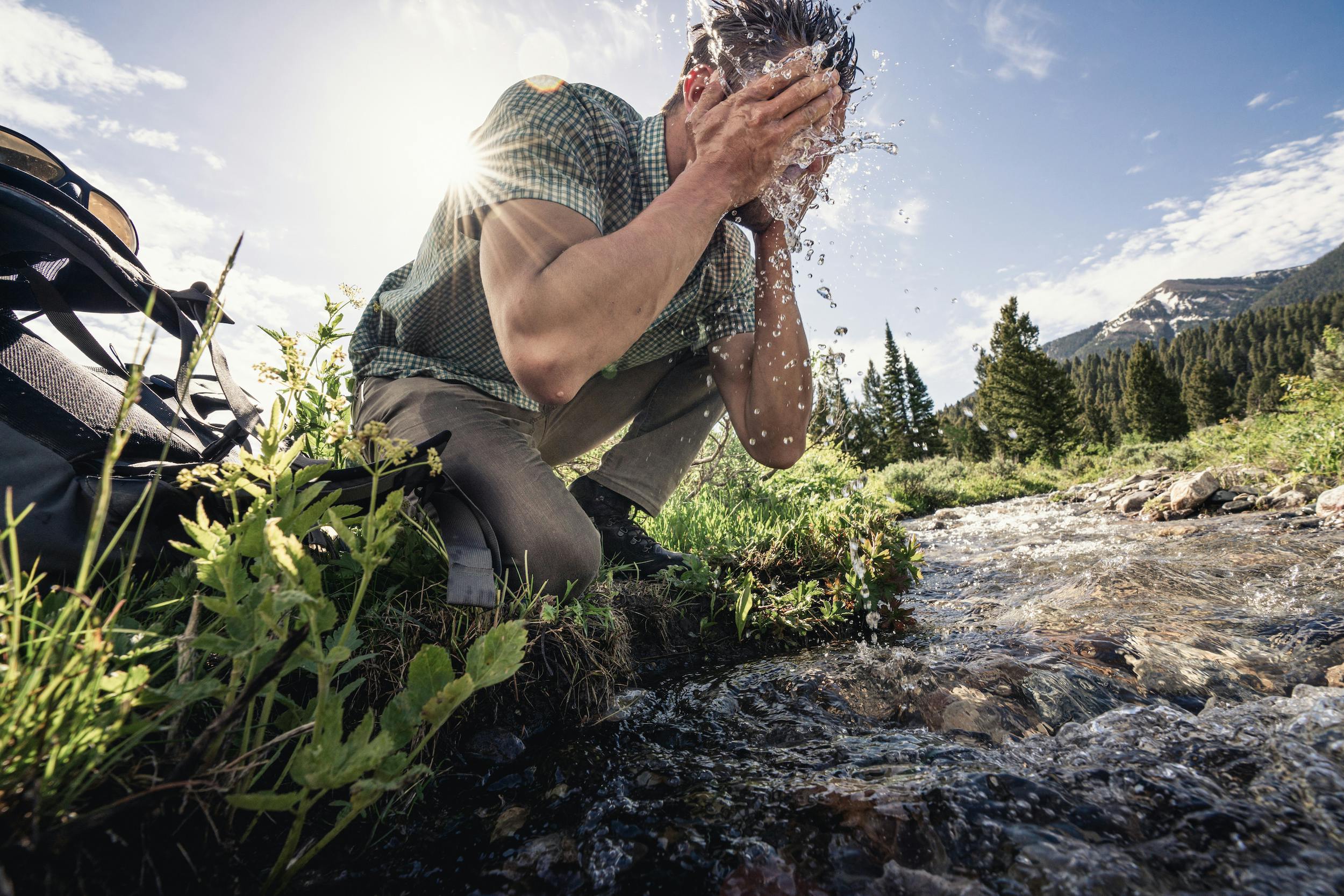 Hiker washing their face in a beautiful mountain creek while on a backpacking trip.