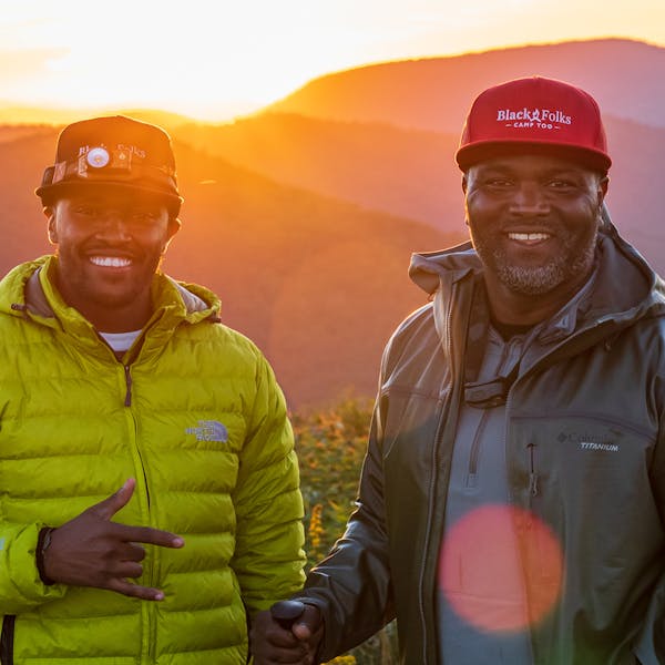 Two hikers with Black Folks Camp Too hats enjoying a beautiful Sunrise in the mountains.