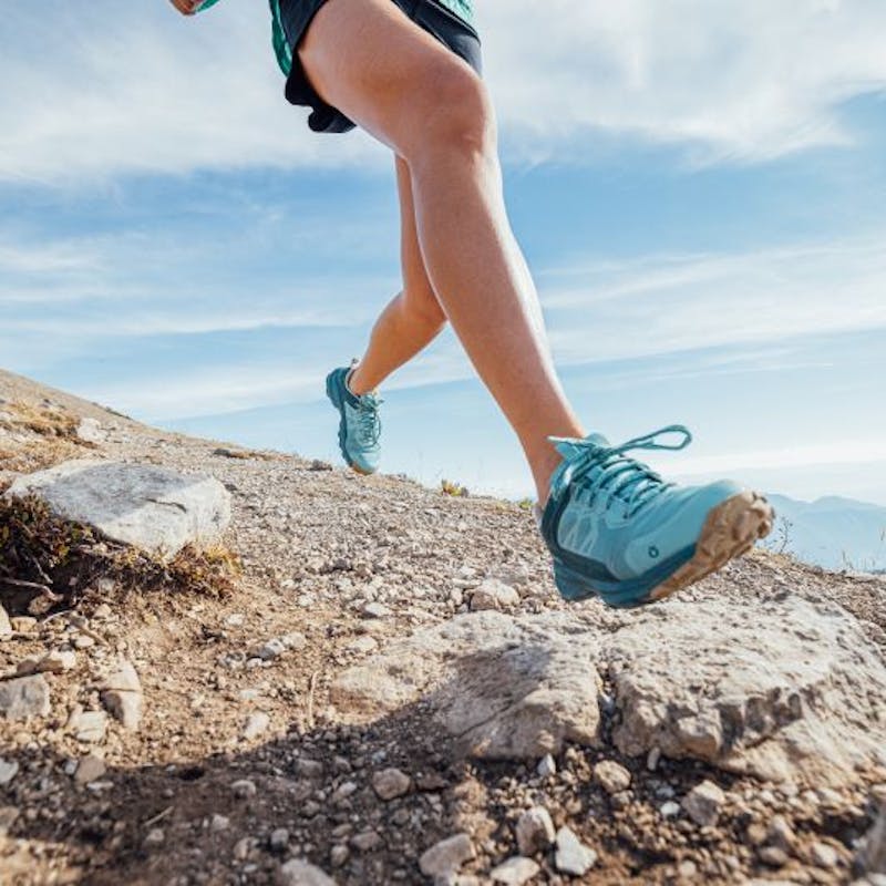 Person running in Oboz Katabatic trail shoes in blue on rocky terrain. 