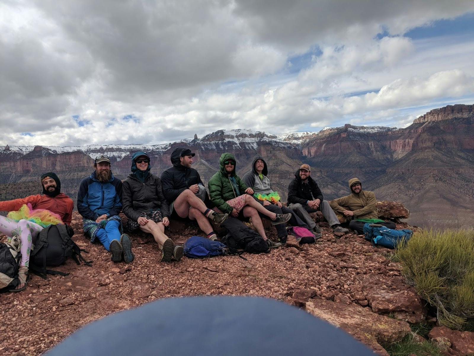 Group of hikers sitting on a bluff overlooking beautiful mountain range behind them