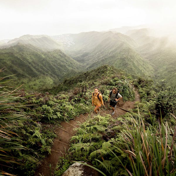 Two hikers climbing to the top of a peak in the rainforest of Hawaii in Oboz hiking boots.