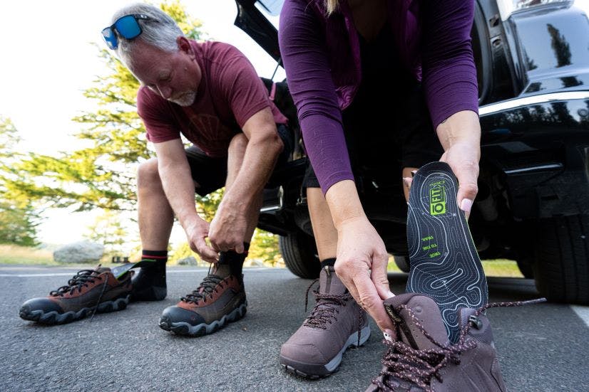 A couple sits on a tailgate tying their Oboz hiking shoes with O FIT insole in preparation for a hike.