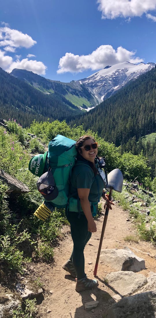 Backpacker carrying a shovel to help work on a trail in the mountains in Oboz Arete hiking boots.