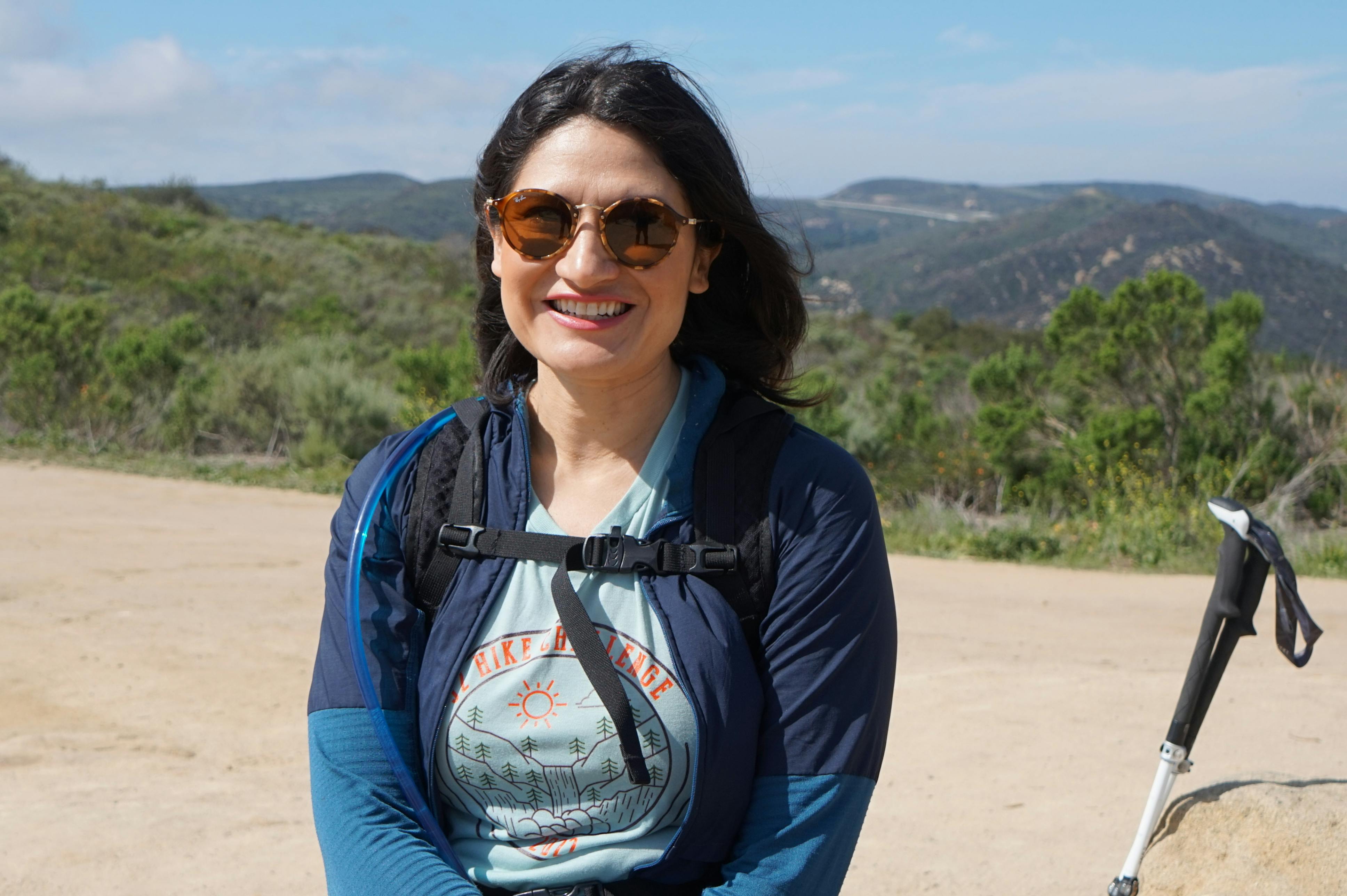 Karla Amador smiling while on a hike in the mountains with some trekking poles.