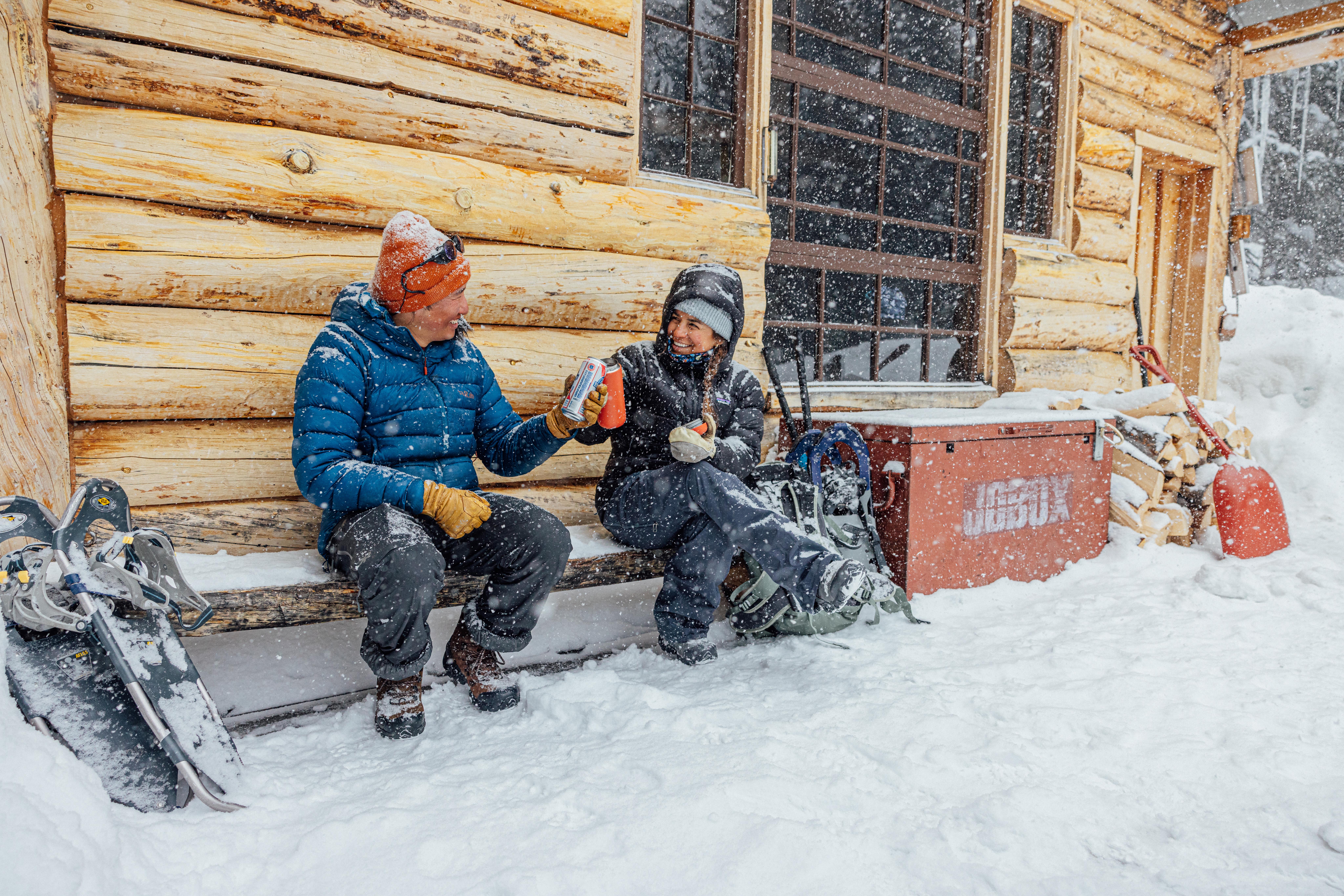 Two winter hikers smile and cheers beers while snowshoeing on a snowy day wearing Oboz Insulated hiking shoes