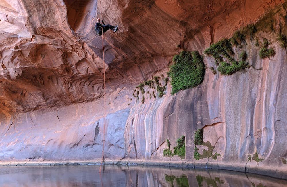 Human repelling down from a canyon wall toward a pool of water