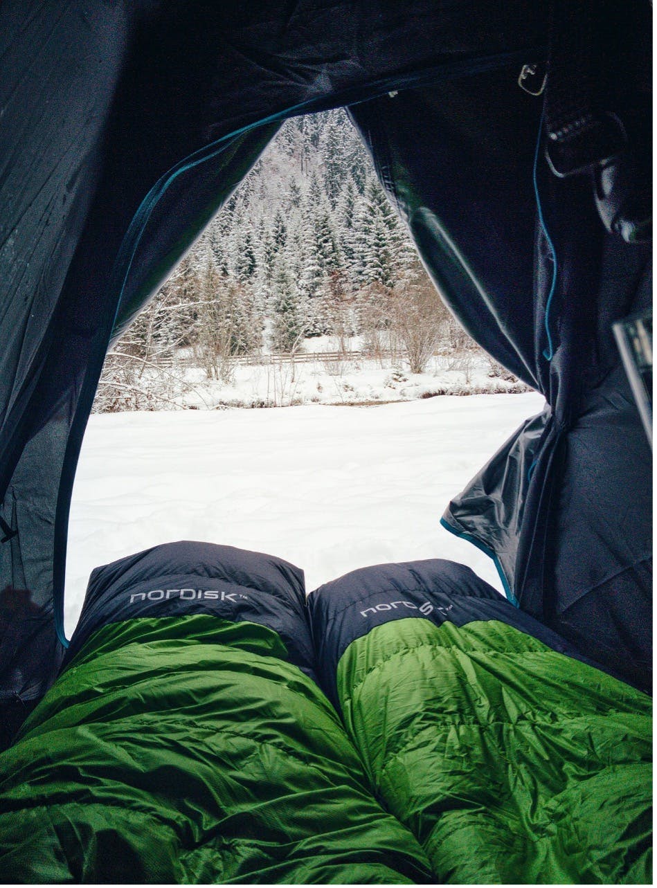 Two people staying warm in sleeping bags on a wintertime camping trip.