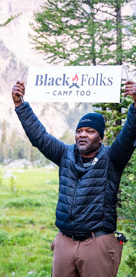 Earl Hunter Jr, founder of Black Folks Camp Too in the wilderness holding a BFCT sign.