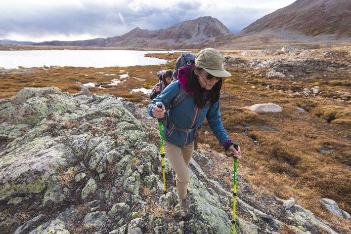 Person hikes in rugged, rocky terrain with treking poles in Oboz hiking shoes. 