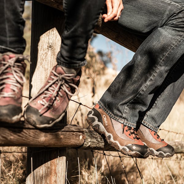 Two people sitting on a fence wearing the Oboz Firebrand II shoes.