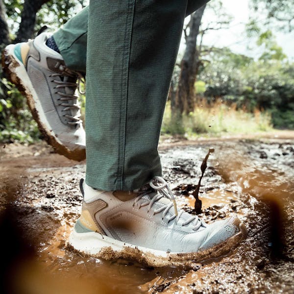 Woman walks through a muddy puddle while hiking a muddy trail in the tropical forest of Hawaii.