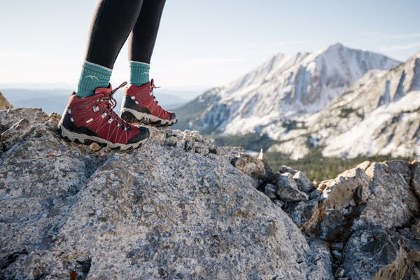 Person wearing Oboz Bridger hiking boot in Rio Red with blue socks on a rocky mountain top.