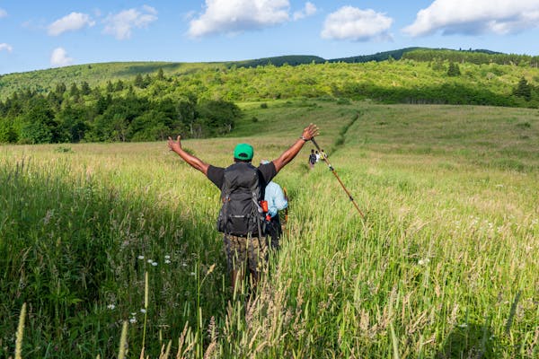 Hiker is raising hands victoriously while walking through a grassy plain