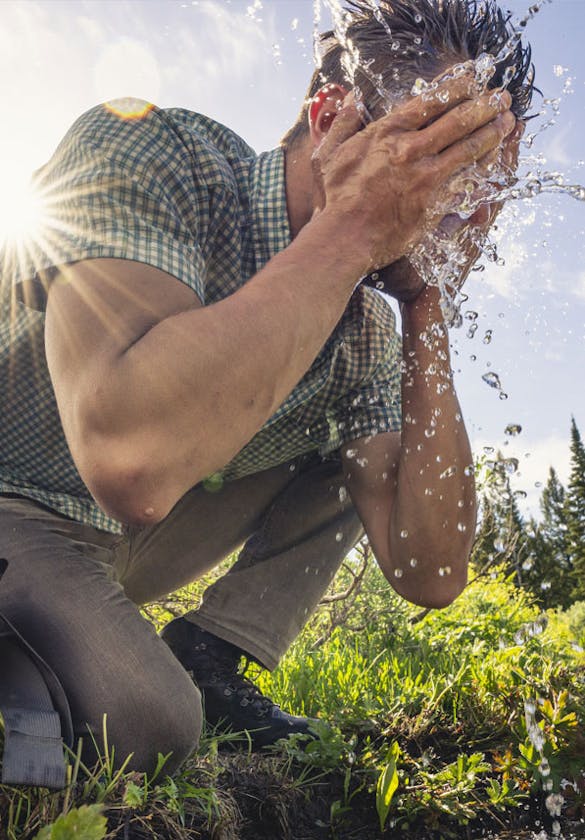 Man splashing water on his face by a mountain stream while wearing Oboz boots on a hike.