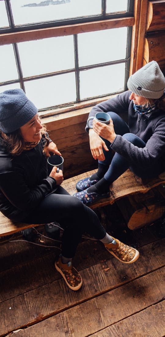 Corinne Prevot, founder of Skida enjoying a conversation in a cabin wearing Oboz Whakata Puffy slippers.
